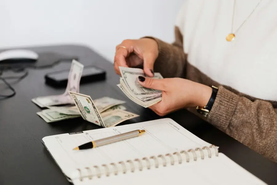 A woman is planning the couple's budget by counting money with an open agenda in front of her, representing How to Manage Finances as a Couple.